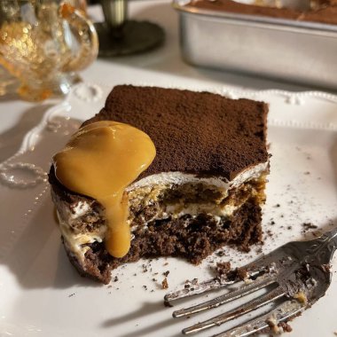 Yumuşak ve kremalı tiramisu dilimi, zengin mascarpone, espressoya batırılmış kadın parmakları ve kakao tozu ile kaplı, her ısırıkta mükemmel bir tatlılık dengesi ve koyu kahve tadı sunuyor..