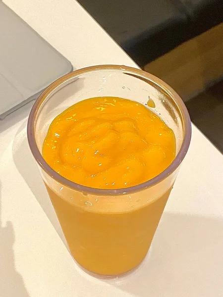 Canlı turuncu-sarı renkli taze mango suyu, bir bardakta servis edilir, pürüzsüz dokusunu sergiler, tropikal aromasını gösterir, ve doğal olarak tatlı ferahlatıcı tadı güneşli bir gün için mükemmel.