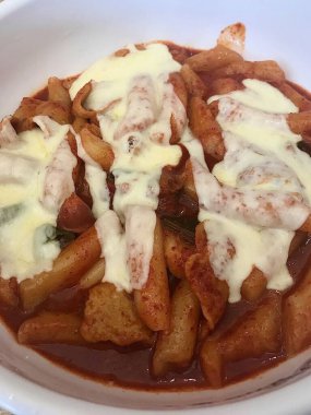 Çiğnenmiş kırmızı soslu pirinç kekleri ve susam tohumları ve yeşil soğanla kaplı baharatlı Kore tteokbokki. Bağımlılık yaratan tadı ve tatmin edici dokusuyla bilinen popüler bir sokak yemeği..