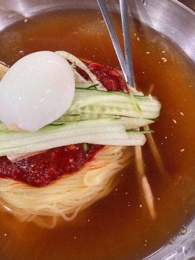 Chilled, chewy naengmyeon noodles in tangy broth paired with juicy, savory mandu dumplings, offering a perfect balance of refreshing coolness and hearty comfort in every delicious Korean bite.