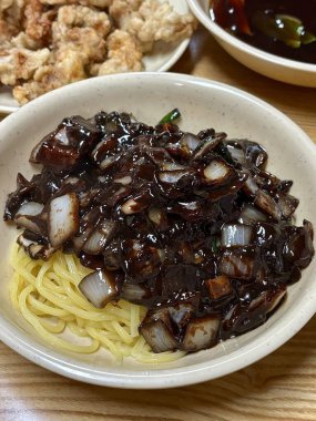 Bol siyah fasulye soslu kalın erişteli klasik jajangmyeon. Dilimlenmiş salatalık ve susam tohumlarıyla süslenmiş. Çok sevilen bir Kore-Çin konfor yemeği, lezzet ve derinlik dolu..
