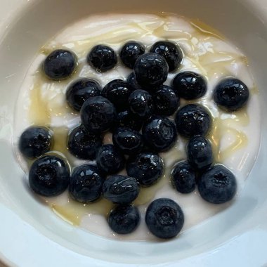 Taze renkli meyvelerle kaplı bir kasede servis edilen Yunan yoğurdu, kremalı pürüzsüz bir doku, canlı doğal renkler ve detaylı bir şekilde ferahlatıcı bir görünüş sunuyor.