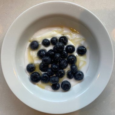 Taze renkli meyvelerle kaplı bir kasede servis edilen Yunan yoğurdu, kremalı pürüzsüz bir doku, canlı doğal renkler ve detaylı bir şekilde ferahlatıcı bir görünüş sunuyor.