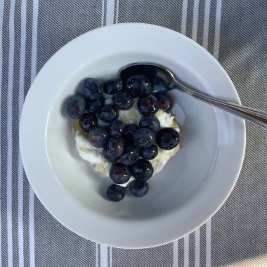 Taze renkli meyvelerle kaplı bir kasede servis edilen Yunan yoğurdu, kremalı pürüzsüz bir doku, canlı doğal renkler ve detaylı bir şekilde ferahlatıcı bir görünüş sunuyor.
