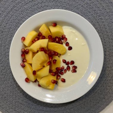 Taze renkli meyvelerle kaplı bir kasede servis edilen Yunan yoğurdu, kremalı pürüzsüz bir doku, canlı doğal renkler ve detaylı bir şekilde ferahlatıcı bir görünüş sunuyor.