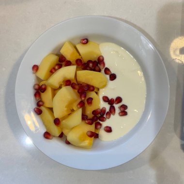 Taze renkli meyvelerle kaplı bir kasede servis edilen Yunan yoğurdu, kremalı pürüzsüz bir doku, canlı doğal renkler ve detaylı bir şekilde ferahlatıcı bir görünüş sunuyor.