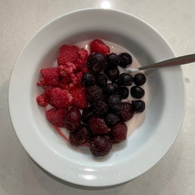 Taze renkli meyvelerle kaplı bir kasede servis edilen Yunan yoğurdu, kremalı pürüzsüz bir doku, canlı doğal renkler ve detaylı bir şekilde ferahlatıcı bir görünüş sunuyor.