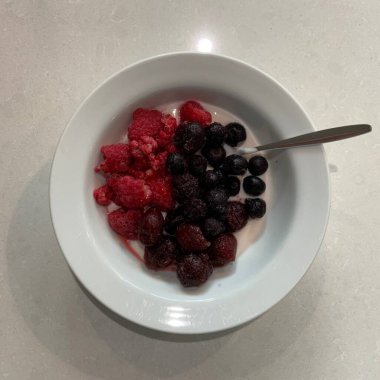 Taze renkli meyvelerle kaplı bir kasede servis edilen Yunan yoğurdu, kremalı pürüzsüz bir doku, canlı doğal renkler ve detaylı bir şekilde ferahlatıcı bir görünüş sunuyor.