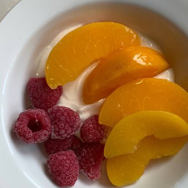 Taze renkli meyvelerle kaplı bir kasede servis edilen Yunan yoğurdu, kremalı pürüzsüz bir doku, canlı doğal renkler ve detaylı bir şekilde ferahlatıcı bir görünüş sunuyor.