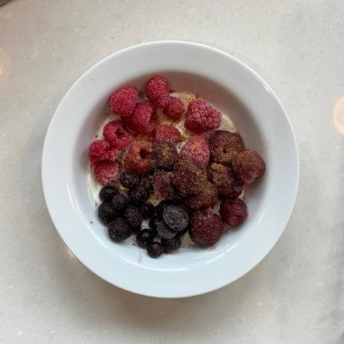 Taze renkli meyvelerle kaplı bir kasede servis edilen Yunan yoğurdu, kremalı pürüzsüz bir doku, canlı doğal renkler ve detaylı bir şekilde ferahlatıcı bir görünüş sunuyor.