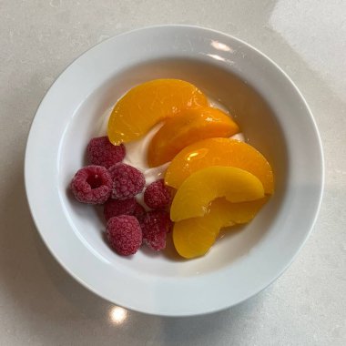 Taze renkli meyvelerle kaplı bir kasede servis edilen Yunan yoğurdu, kremalı pürüzsüz bir doku, canlı doğal renkler ve detaylı bir şekilde ferahlatıcı bir görünüş sunuyor.