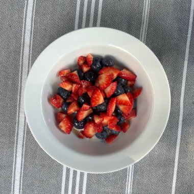 Taze renkli meyvelerle kaplı bir kasede servis edilen Yunan yoğurdu, kremalı pürüzsüz bir doku, canlı doğal renkler ve detaylı bir şekilde ferahlatıcı bir görünüş sunuyor.