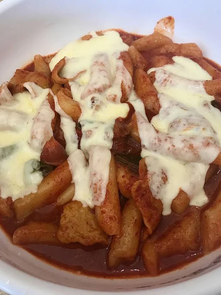 Çiğnenmiş kırmızı soslu pirinç kekleri ve susam tohumları ve yeşil soğanla kaplı baharatlı Kore tteokbokki. Bağımlılık yaratan tadı ve tatmin edici dokusuyla bilinen popüler bir sokak yemeği..