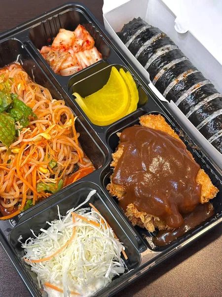 Geleneksel bir Kore dozirak 'ı. Pirinç, çeşitli banchan ve tuzlu proteinlerle güzelce düzenlenmiş. Dengeli ve görsel olarak davetkâr, canlı lezzetlerle dolu taşınabilir bir yemek..