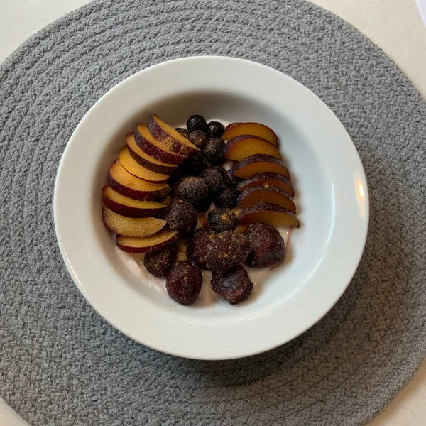 Taze renkli meyvelerle kaplı bir kasede servis edilen Yunan yoğurdu, kremalı pürüzsüz bir doku, canlı doğal renkler ve detaylı bir şekilde ferahlatıcı bir görünüş sunuyor.