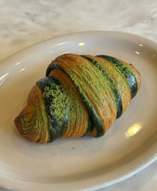 Pul pul, altın kruvasan ve canlı yeşil kibrit çöpü. Zarif bir şekilde beyaz krema serpiştirilmiş. Moda kafe ve tatlı fotoğrafçılığı için modern bir füzyon hamur işi..