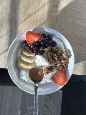 Taze meyve ve çıtır çıtır malzemelerle kaplı kremalı yoğurt kasesi pürüzsüz bir doku ve ferahlatıcı bir tat sunuyor. Hafif, sağlıklı ve görsel olarak çekici, kahvaltı ya da sağlıklı atıştırmalıklar için mükemmel..