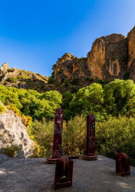 Suspension Bridge Anchors Beneath Dramatic Cliffs in a Sunlit Mountain Gorge