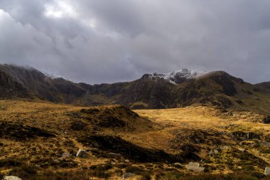 Karla kaplı tepeler ve karlı gökyüzü ile dramatik Galler Dağı manzarası