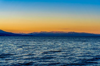 Ohri Gölü 'nün Üzerinde Altın Gün Batımı Uzaktaki Karla kaplı Dağlar ve Sakin Mavi Su