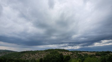 Geniş yatay manzara, Fransa 'nın Quercy bölgesindeki tepelik, yeşil ve çalılık arazi üzerinde yoğun, çalkantılı, koyu gri fırtına bulutlarını gösteriyor..