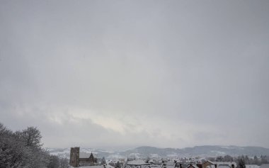 Minimalist winter background. A silhouette of a snow-covered French town with a church tower sits at the bottom, leaving a vast grey sky for text.