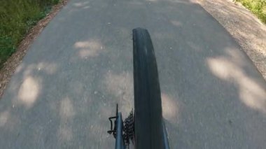 Dinamik bakış açısı, yavaş çekim güneşli bir asfalt yolda parktan ya da ormandan geçen bir bisiklet lastiğini gösteriyor. Hareket ve eyleme odaklan.