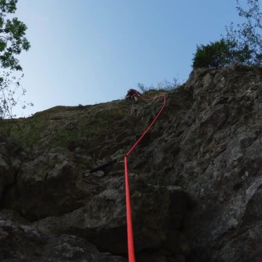 Kaya tırmanışçısı, öğleden sonra güneşinde sarp kayalıkların üzerinde ip bağlıyor.