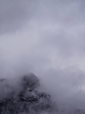 Minimalist kış arka planında kalın, açık gri bulut örtüsüyle kaplı bir dağın karanlık, tozlu dış hatları büyük bir kopya alanı sunuyor..