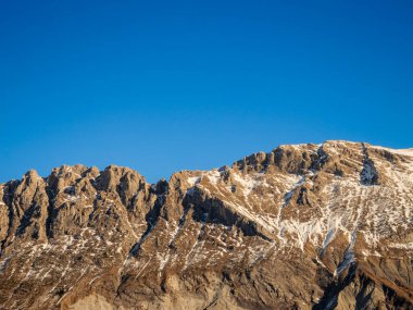 Kayalık dağ zirvelerinin panoramik bir görüntüsü ılık ışıkla yıkanmış engin, açık mavi bir gökyüzü arkaplanı, kopyalama alanı için mükemmel..