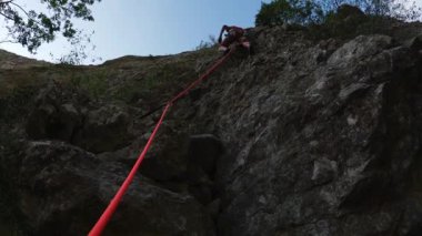 Kaya tırmanışçısı, Kırmızı İp ve Mavi Gökyüzü ile Dik Uçuruma Yükseliyor