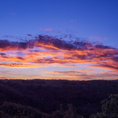 Göz kamaştırıcı renkli bir gün batımı. Derin, mavi bir gökyüzüne karşı yatay, turuncu ve pembe bulutların oluşturduğu yatay çizgiler..