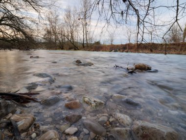 Sakin ve huzurlu bir nehir taşları üzerinde akan temiz su manzarası. Sakin bir kıyıda kış günbatımında..