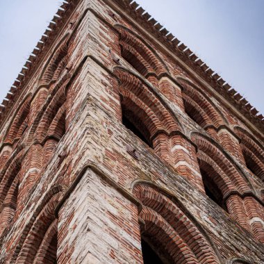 Alternatif kırmızı tuğla ve beyaz taş duvar bantlarının yer aldığı tarihi Romanesk çan kulesinin alçak açılı görüntüsü.