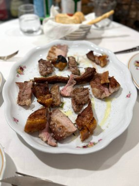 Beyaz bir tabakta barbekü soslu domuz kaburgası ve arka planda salata ve içecek..