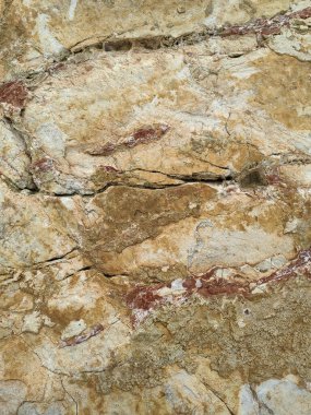 Yıpranmış bir taş yüzeyin detaylı bir yakın çekimi. Toprak bej, pas tonları, organik mineral lekeleri ve doğal dokular soyut, kırsal bir desen oluşturuyor..