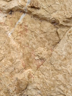 Yıpranmış bir taş yüzeyin detaylı bir yakın çekimi. Toprak bej, pas tonları, organik mineral lekeleri ve doğal dokular soyut, kırsal bir desen oluşturuyor..