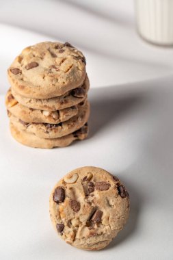 Tek bir çikolata parçalı ve fındıklı kurabiyeye odaklanmış yukarıdan aşağı bir çekim. Bulanık kurabiye yığını bolluğu gösteriyor. Parlak beyaz arkaplan