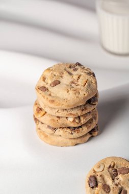 Arka planda bulanık bir bardak süt ve köşede de görünen bir kurabiye yığını.