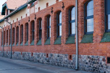 Tuğla binanın bir sürü penceresi ve yeşil süslemesi var. Pencereler büyük ve bina eski.