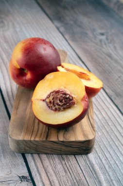 Yakından, dikey bir kompozisyonda bütün bir nektarin ve yarıya indirgenmiş, sulu iç ve çukur, küçük ahşap bir kesme tahtası üzerinde sergileniyor.