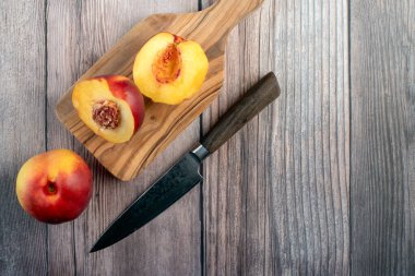 İki yarım nektarin, bir meyve ve ahşap bir arka planda duran doğal zeytin ağacı kesme tahtasının üzerinde bir şefin bıçağı.