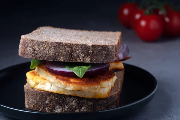 Gurme Halloumi sandviçi arka planda vişneli domatesli siyah bir tabakta servis edilir. Akdeniz diyet ilhamı.