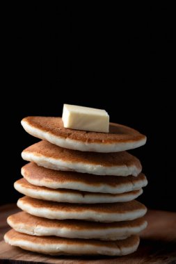 Üzerinde bir parça tereyağı ve siyah bir arkaplan olan bir yığın pofuduk krepin dikey çekimi. Salı gününü kısalt