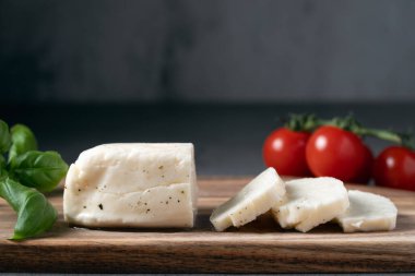 Tahtada beyaz halloumi peyniri dilimleri, kiraz domatesleri ve fesleğen yapraklarıyla.