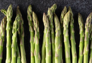 Taze organik kuşkonmaz sapları dikey olarak koyu taştan bir yüzeye dizilmiştir.