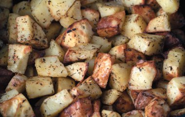 Kurutulmuş otlar ve kırmızı baharatlarla tatlandırılmış altın sarısı fırın fırınlı patatesler.