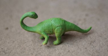 Minyatür yeşil Brachiosaurus dinozor oyuncak heykelciği kumlu zeminde. Gerçekçi deri dokusuna sahip uzun boyunlu plastik dinozor oyuncağının yan profili