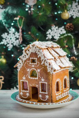 Noel ağacı arkaplanındaki ahşap masa üzerinde jöleli zencefilli kurabiye evi ve kapağı yanan çelenkler. Şenlik havası. Noel sabahı. Zencefilli kurabiye evi.