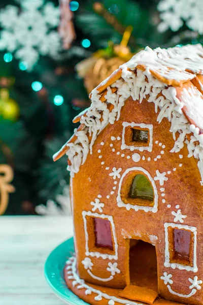 Christmas Gingerbread House with glaze On Wooden Table On Background Of Christmas Tree With Burning Garlands Close Up. Festive mood. Christmas morning. Gingerbread house